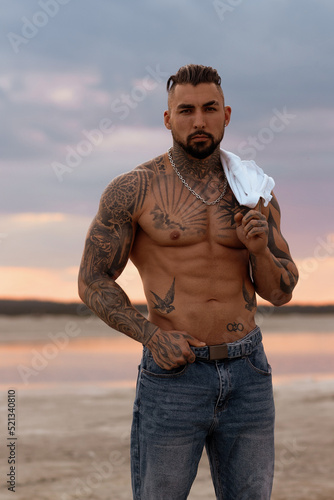 Handsome young muscular italian man posing shirtless on the beach, sunset summer time