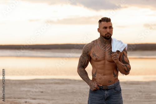 Handsome young muscular italian man posing shirtless on the beach, sunset summer time