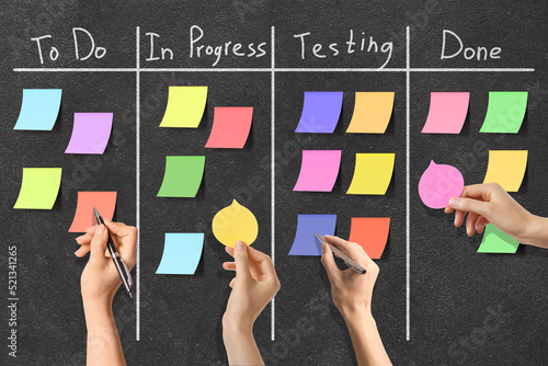 Hands attaching sticky notes to scrum task board photo