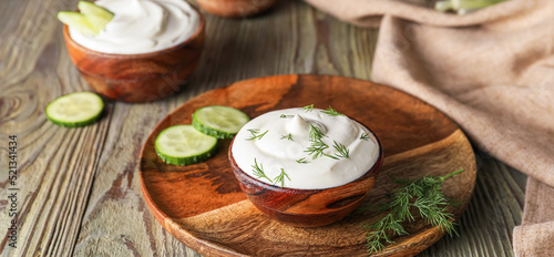 Bowls of tasty sour cream and dill on wooden background