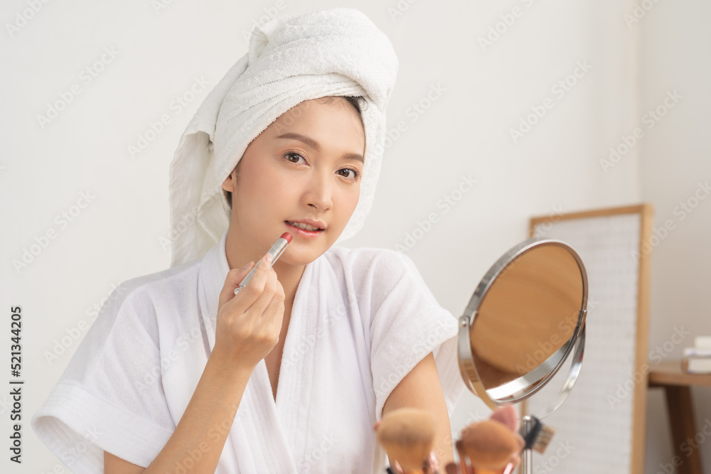 Beauty cosmetics concept, asian young woman, girl in bathrobe, towel after shower bath at home make up face by applying lipstick, lips on her mouth, looking at the mirror, fashion style, skin care. Beauty cosmetics concept, asian young woman, girl in bathrobe, towel after shower bath at home make up face by applying lipstick, lips on her mouth, looking at the mirror, fashion style, skin care.