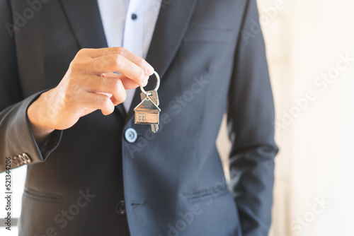 Home agent, broker man in suit standing, realtor holding the house key to hand over to new homeowner or tenant , client after the bank approved the home loan, mortgage loan. Property lease of landlord