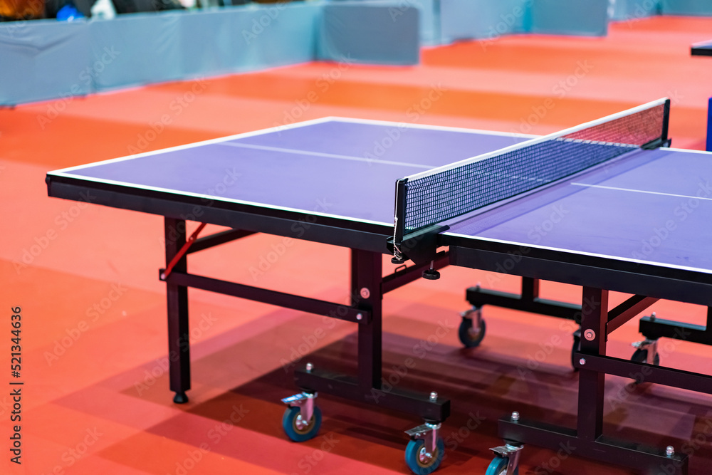 Blue table tennis or pingpong table is settle on a red, orange floor of the indoor court stadium for competitions tournament.