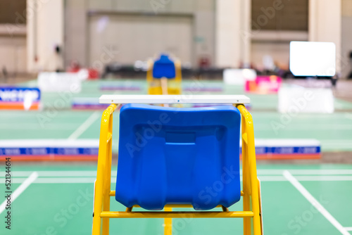 Blue chair of badminton referee with yellow colors near badminton net with blurred background in sport indoor stadium. photo