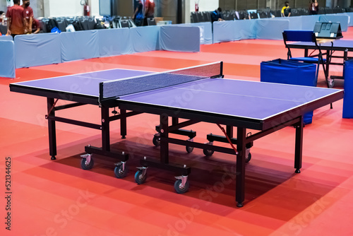Blue table tennis or pingpong table is settle on a red, orange floor of the indoor court stadium for competitions tournament. © Surachetsh