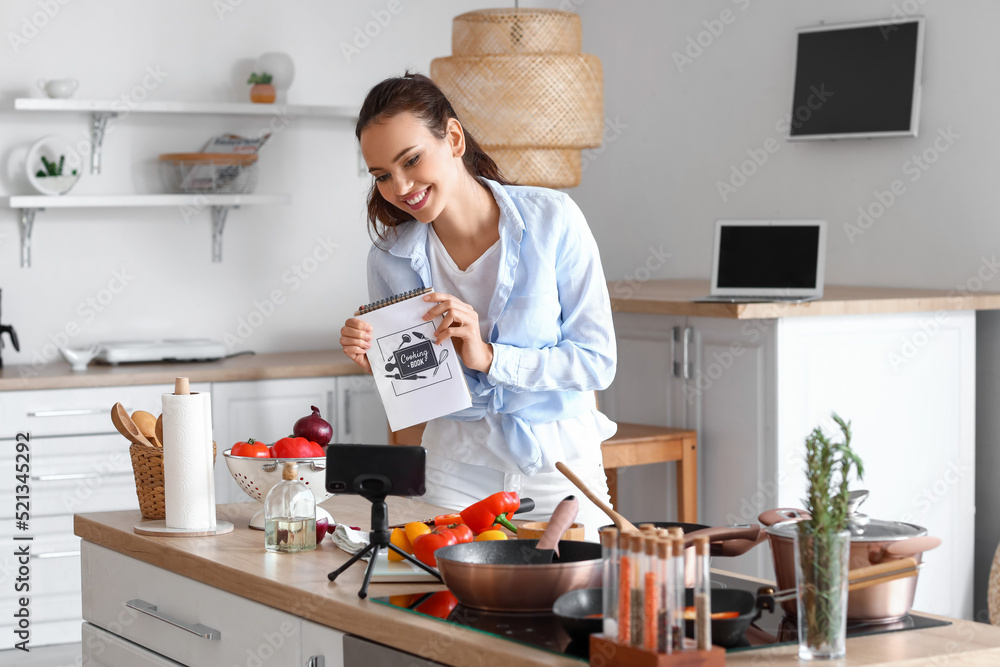 Young woman with cooking book recording video tutorial in kitchen Young woman with cooking book recording video tutorial in kitchen