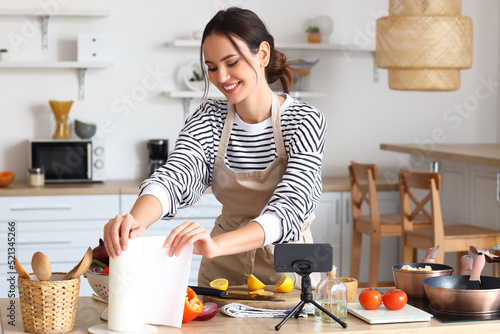 Young woman taking paper towel while following cooking video tutorial in kitchen photo