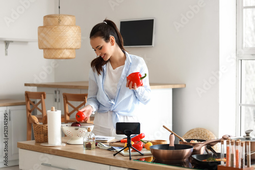 Young woman with vegetables recording cooking class in kitchen