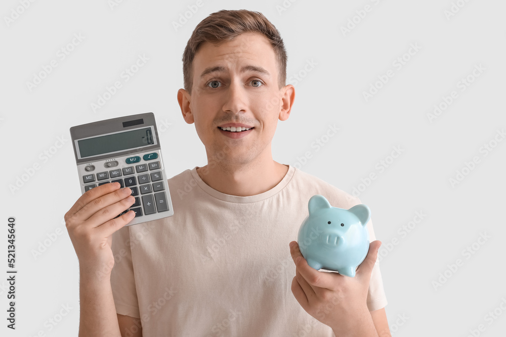 Young man with blue piggy bank and calculator on white background Young man with blue piggy bank and calculator on white background