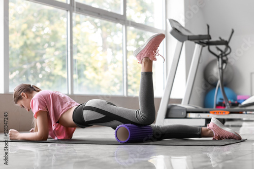 Young woman exercising with foam roller in gym