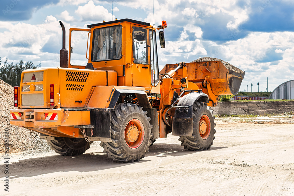 A large front loader transports crushed stone or gravel in a bucket at a construction site or concrete plant. Transportation of bulk materials. Construction equipment. Bulk cargo transportation.