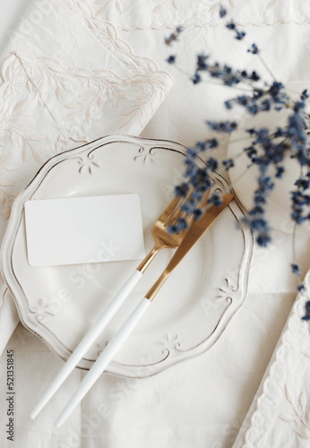 Blank paper sheet card mockup on minimal table place setting top view on beige linen tablecloth and lavender flowers in a vase.  Space for text. Wedding invitation, menu. Provence  style.