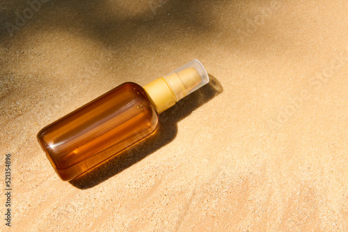 Top view. Minimalist still life of unbranded dark glass bottle with SPF oil or sunscreen body lotion on golden sand beach background. Summer cosmetic concept. Copy ad space for promotional text