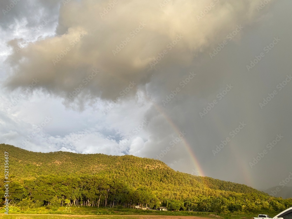 Rainbow and rainstorm sky over mountain and forest.