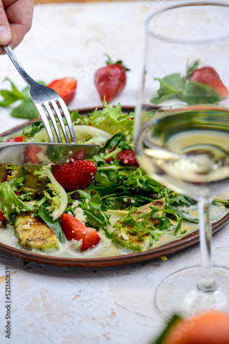 fresh salad with grilled avocado and strawberries and couscous porridge in a clay plate with utensils in hand 