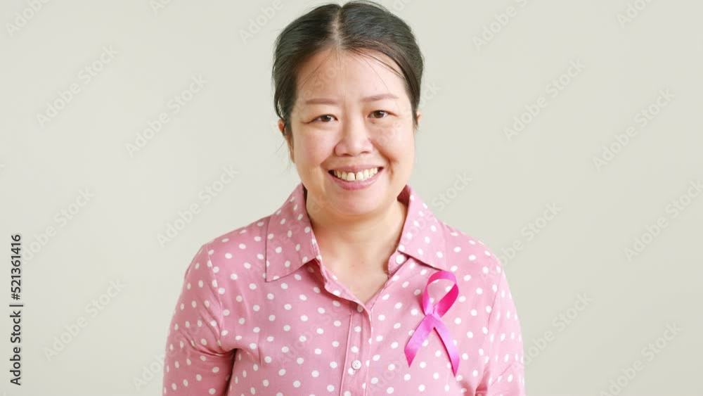 Portrait of young Asian woman in pink shirt with pink ribbon smiling on gray background for October breast cancer awareness month Portrait of young Asian woman in pink shirt with pink ribbon smiling on gray background for October breast cancer awareness month
