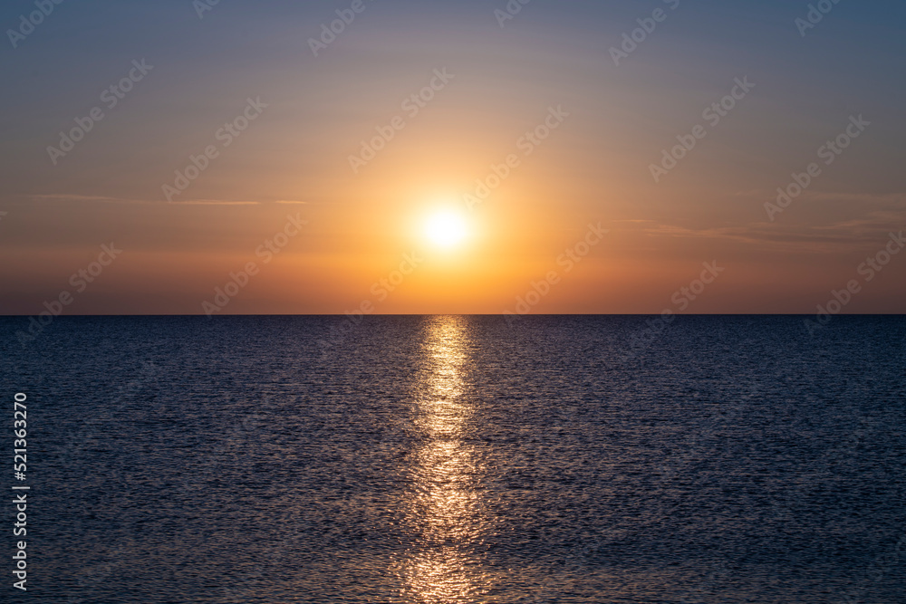 Beautiful Sunset with large yellow sun over mediterranean sea. Deep blue water and orange sky.