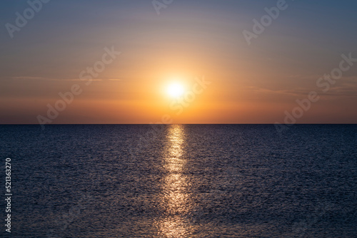 Beautiful Sunset with large yellow sun over mediterranean sea. Deep blue water and orange sky.