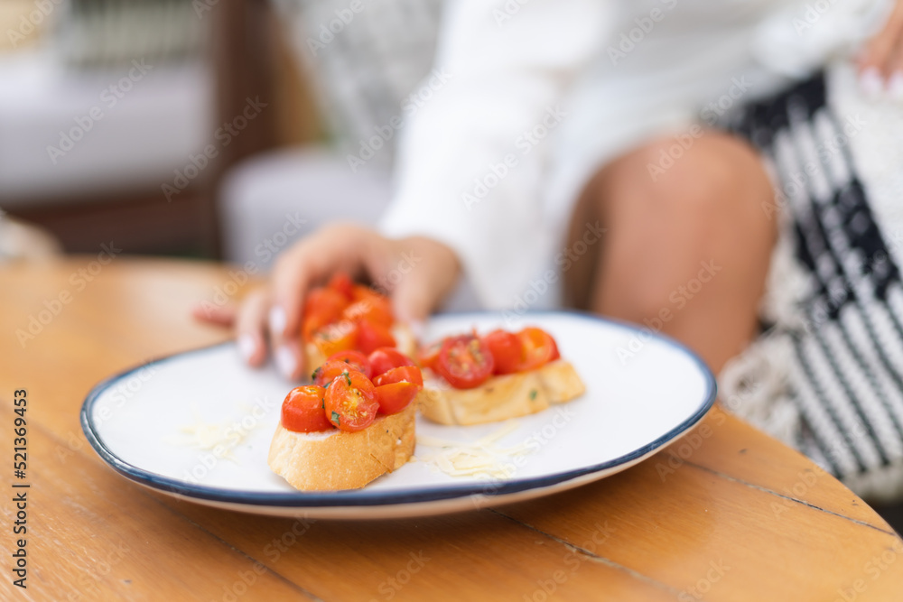 Close shot of a dish with bruschettas with tomatoes in a summer cafe, a girl in an elegant dress takes a bruschetta