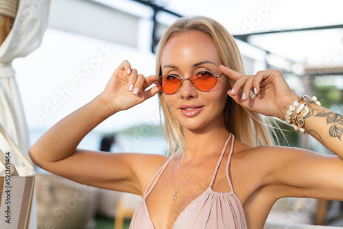 Beautiful young elegant girl in a pink dress and orange stylish glasses in a summer tropical cafe, romantic, tender, positive
