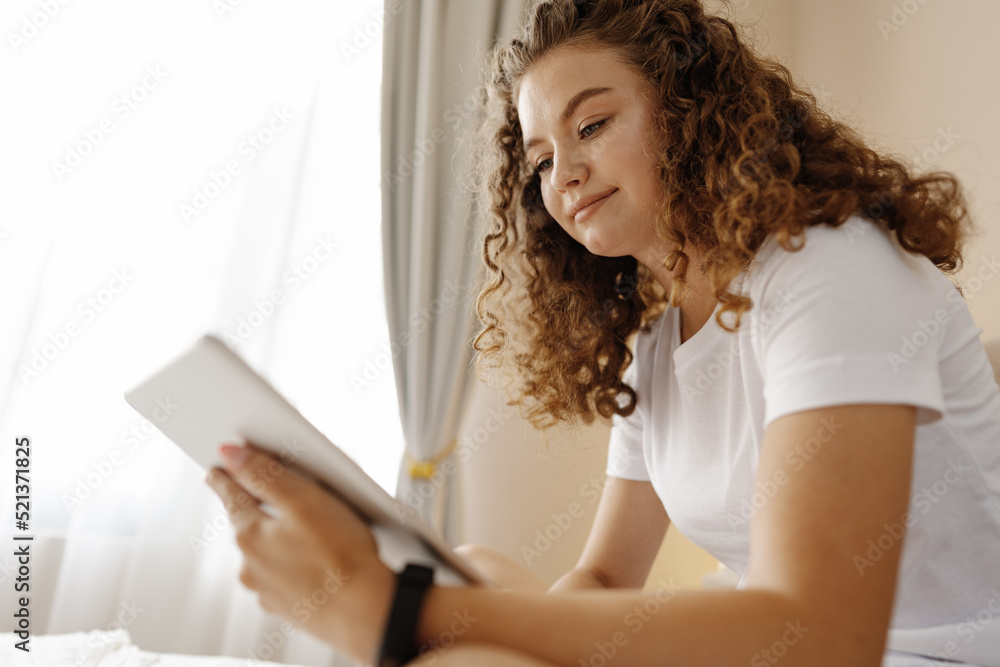 Portrait of young woman using modern digital tablet sitting on a bed Portrait of young woman using modern digital tablet sitting on a bed