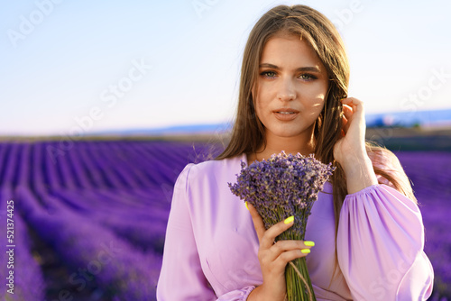 Young woman in dress holding bouquet of flowers standing in lavender field