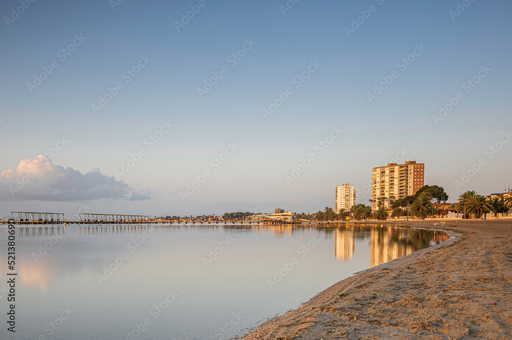 Naklejka premium High rise building, along a Spanish beach, reflecting in the calm ocean, at sunrise