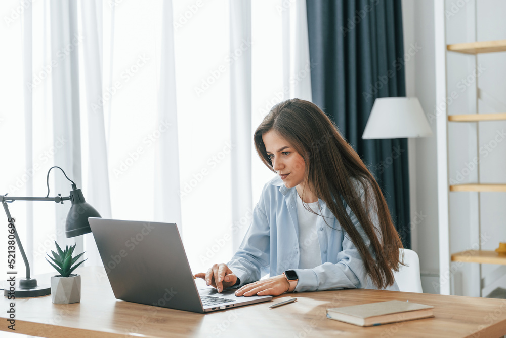 Freelance worker is sitting by table with laptop. Young beautiful woman is home alone in domestic room Freelance worker is sitting by table with laptop. Young beautiful woman is home alone in domestic room