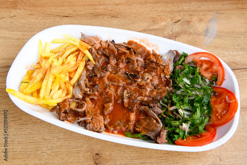 Turkish and Arabic Traditional Ramadan doner kebab with tasty tomato sauce and rice or turkish pilav in white plate on wood table background. ( Pilav ustu doner) photo