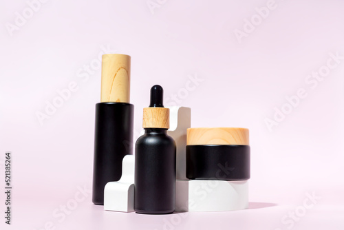Set of black matte glass cosmetics bottles with bamboo lids on the white podium. Mockup background with cocncrete geometric figures and copy space. Stage with product presentation.