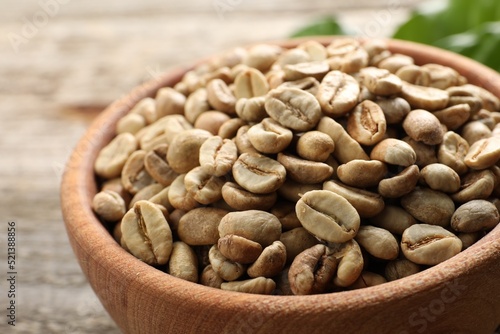 Green coffee beans in wooden bowl on table, closeup