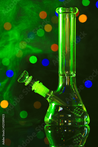 Glass bong with smoke against blurred lights, toned in green. Smoking device