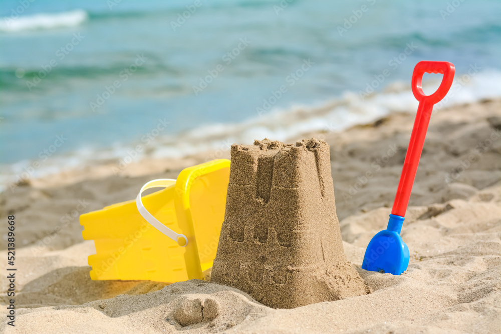 Beautiful sand castle, child plastic shovel and bucket on beach near sea Beautiful sand castle, child plastic shovel and bucket on beach near sea