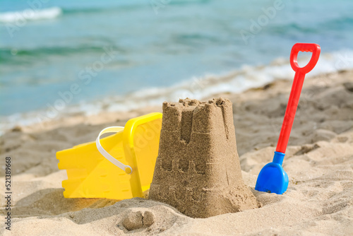 Beautiful sand castle, child plastic shovel and bucket on beach near sea photo
