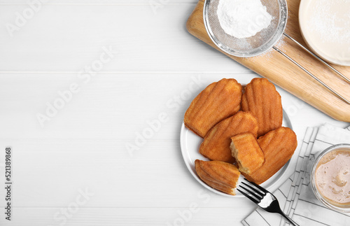 Delicious madeleine cakes, powdered sugar and drink on white wooden table, flat lay. Space for text