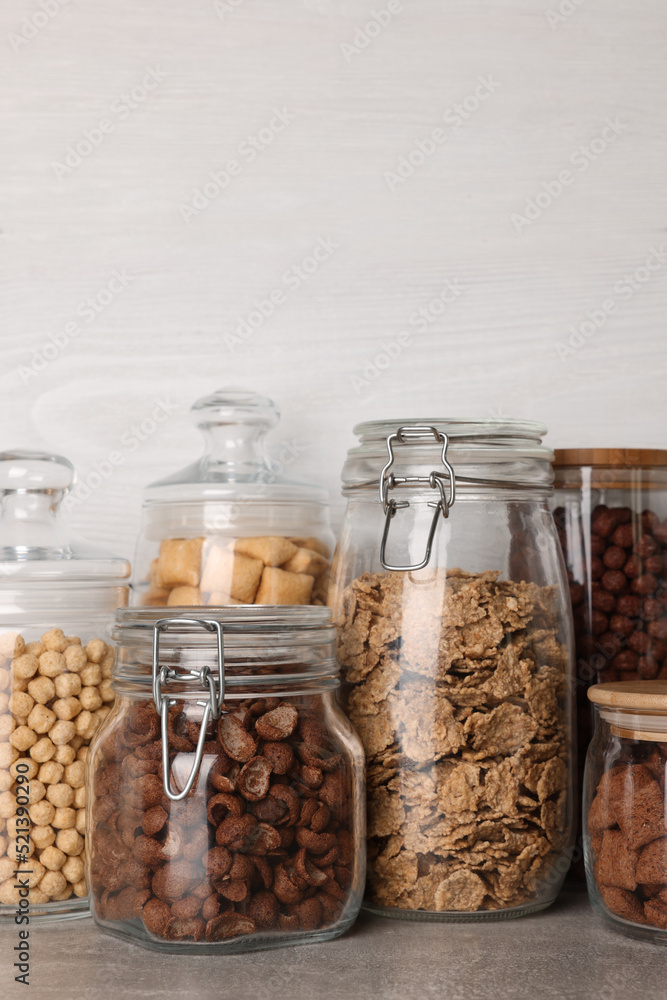 Glass containers with different breakfast cereals on grey countertop near white wooden wall Glass containers with different breakfast cereals on grey countertop near white wooden wall