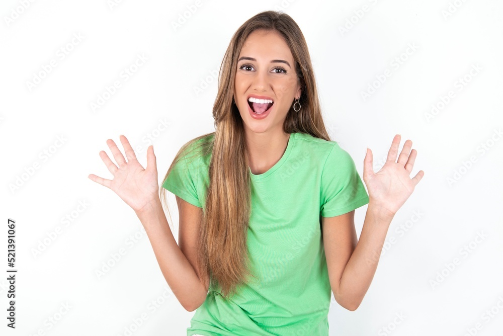Optimistic young beautiful woman wearing green T-shirt over white background raises palms from joy, happy to receive awesome present from someone, shouts loudly, Optimistic young beautiful woman wearing green T-shirt over white background raises palms from joy, happy to receive awesome present from someone, shouts loudly,
