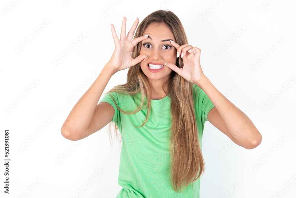young beautiful woman wearing green T-shirt over white background keeping eyes opened to find a success opportunity. young beautiful woman wearing green T-shirt over white background keeping eyes opened to find a success opportunity.