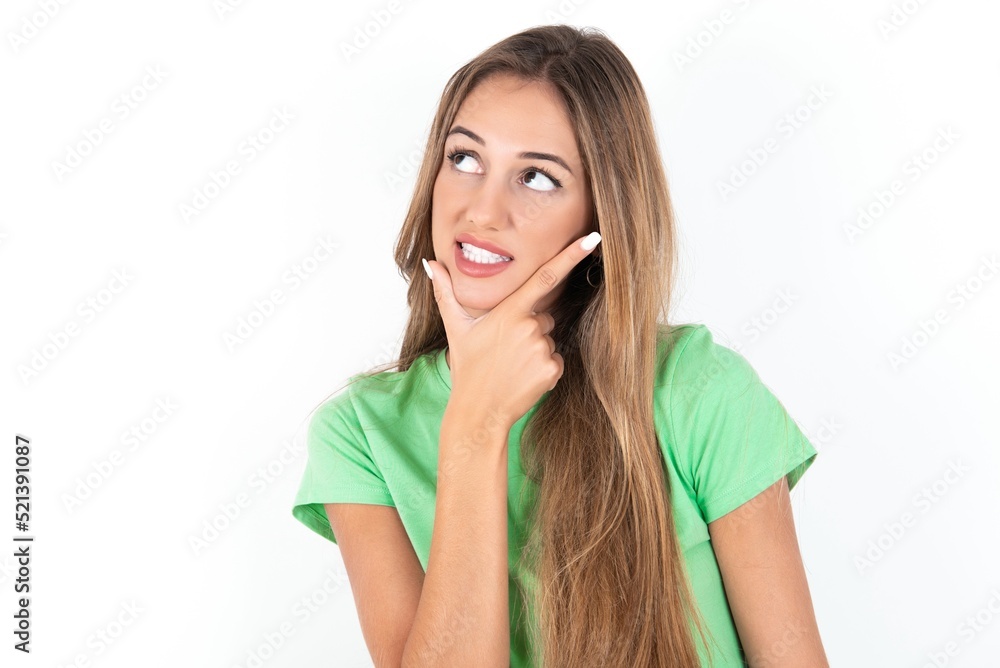 young beautiful woman wearing green T-shirt over white background Thinking worried about a question, concerned and nervous with hand on chin. young beautiful woman wearing green T-shirt over white background Thinking worried about a question, concerned and nervous with hand on chin.