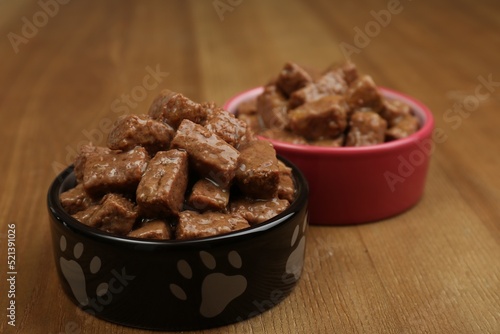 Wet pet food in feeding bowls on wooden background