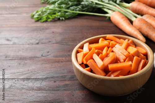 Cut carrot in bowl on brown wooden table, closeup. Space for text