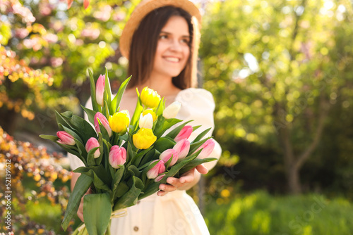 Beautiful young woman with bouquet of tulips in park, focus on flowers. Space for text