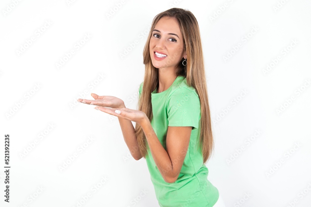 young beautiful woman wearing green T-shirt over white background, pointing aside with hands open palms showing copy space, presenting advertisement smiling excited happy young beautiful woman wearing green T-shirt over white background, pointing aside with hands open palms showing copy space, presenting advertisement smiling excited happy