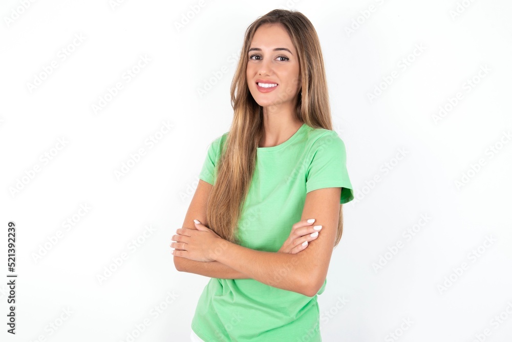 young beautiful woman wearing green T-shirt over white background, happy face smiling with crossed arms looking at the camera. Positive person. young beautiful woman wearing green T-shirt over white background, happy face smiling with crossed arms looking at the camera. Positive person.