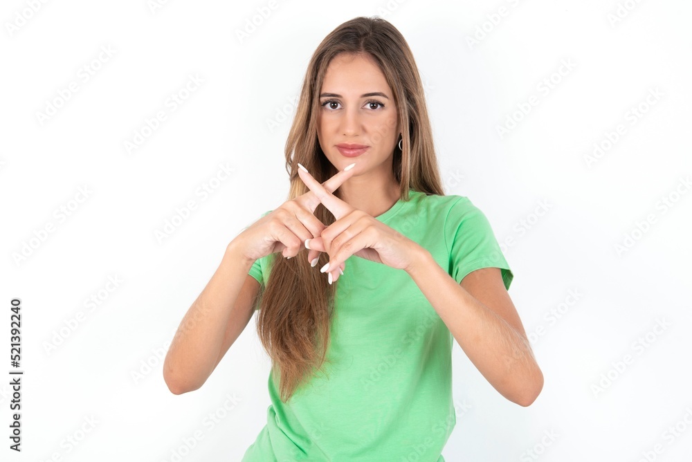 young beautiful woman wearing green T-shirt over white background, Has rejection angry expression crossing fingers doing negative sign. young beautiful woman wearing green T-shirt over white background, Has rejection angry expression crossing fingers doing negative sign.