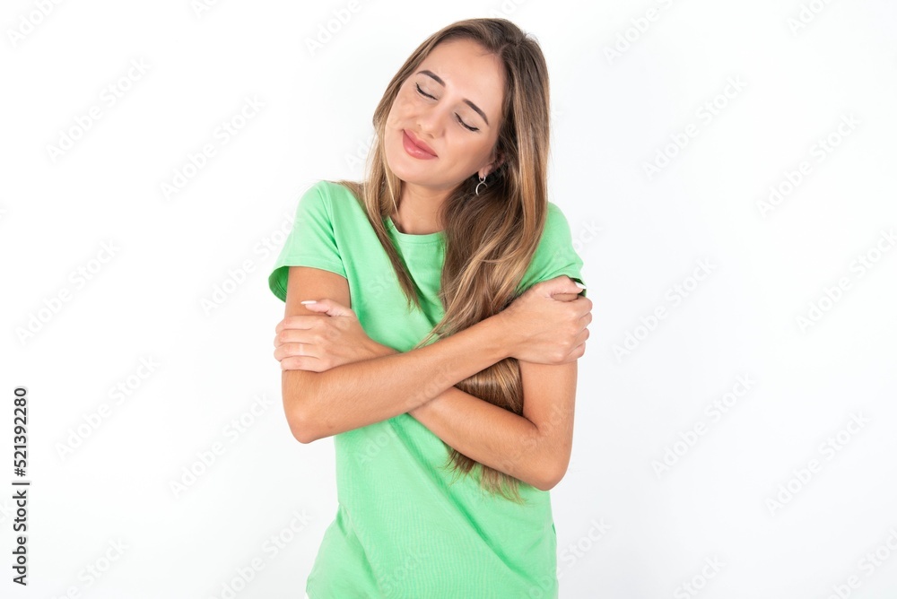 young beautiful woman wearing green T-shirt over white background, Hugging oneself happy and positive, smiling confident. Self love and self care young beautiful woman wearing green T-shirt over white background, Hugging oneself happy and positive, smiling confident. Self love and self care