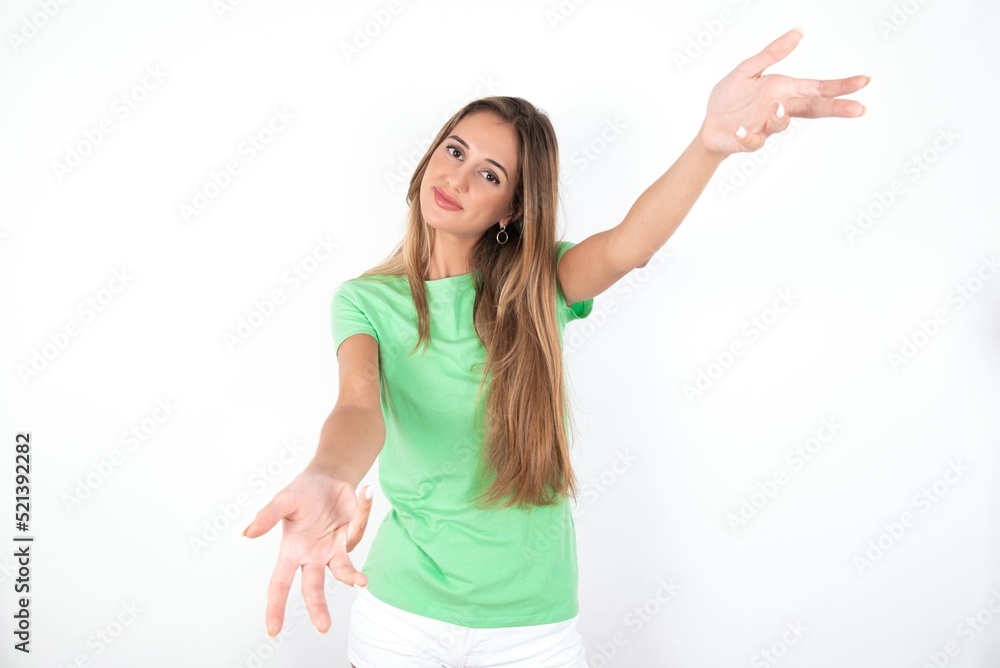 young beautiful woman wearing green T-shirt over white background, looking at the camera smiling with open arms for hug. Cheerful expression embracing happiness. young beautiful woman wearing green T-shirt over white background, looking at the camera smiling with open arms for hug. Cheerful expression embracing happiness.