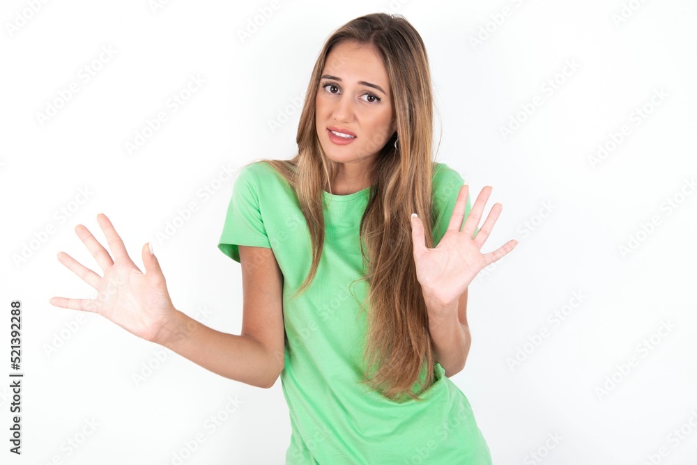 young beautiful woman wearing green T-shirt over white background, afraid and terrified with fear expression stop gesture with hands, shouting in shock. Panic concept. young beautiful woman wearing green T-shirt over white background, afraid and terrified with fear expression stop gesture with hands, shouting in shock. Panic concept.