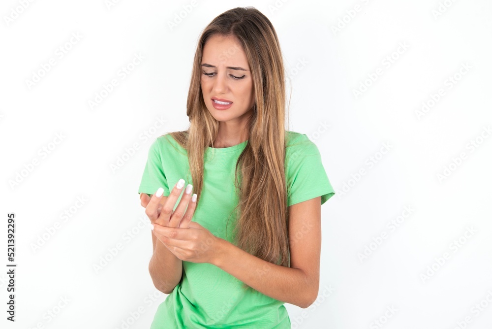 young beautiful woman wearing green T-shirt over white background, Suffering pain on hands and fingers, arthritis inflammation young beautiful woman wearing green T-shirt over white background, Suffering pain on hands and fingers, arthritis inflammation