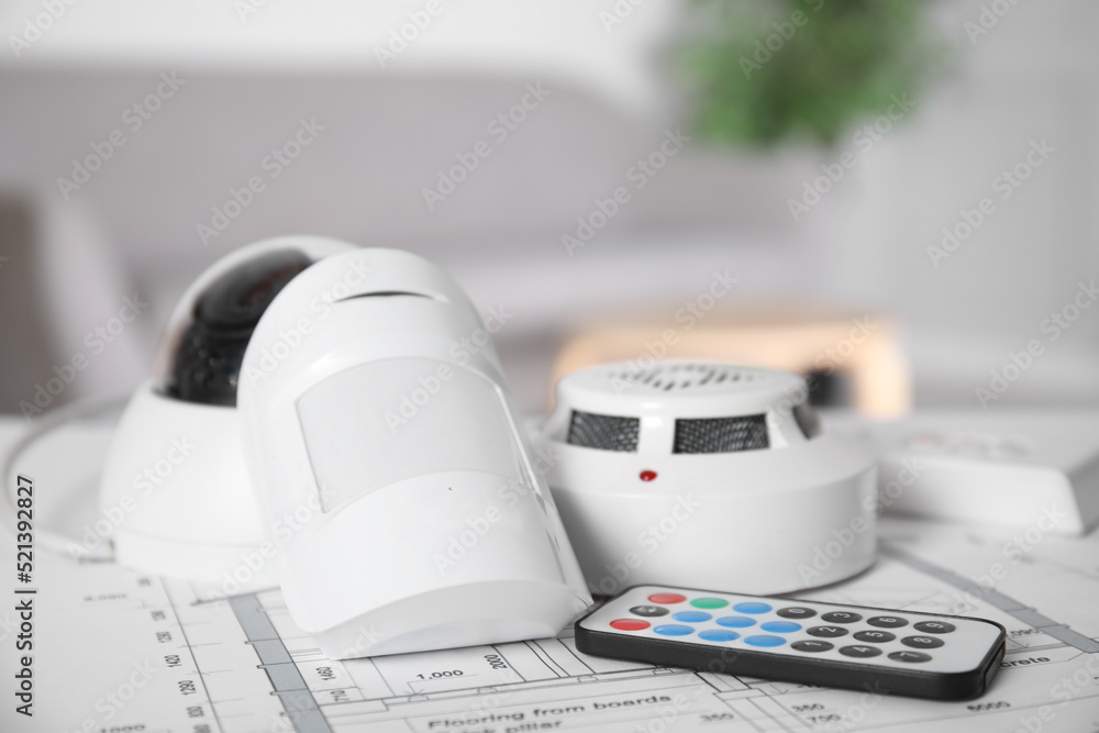 CCTV camera, remote control, smoke and movement detectors on building plan indoors. Home security system CCTV camera, remote control, smoke and movement detectors on building plan indoors. Home security system